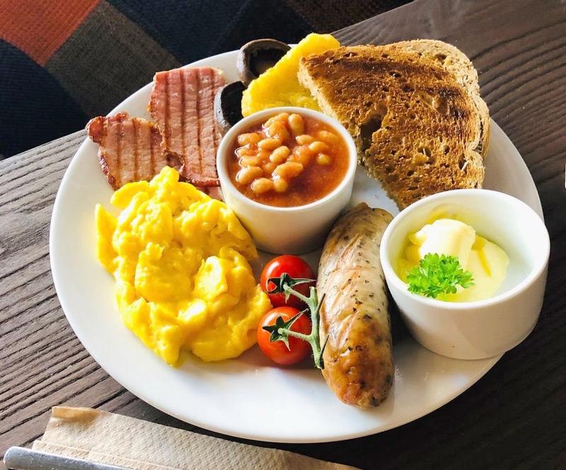 Full English breakfast with scrambled eggs, sausage, bacon, toast, baked beans, tomato, and a soft-boiled egg