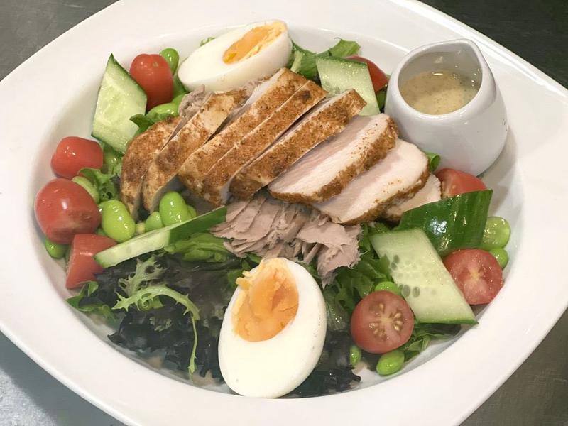 Salad with sliced chicken breast, boiled eggs, tuna, cucumber, cherry tomatoes, edamame beans, and dressing