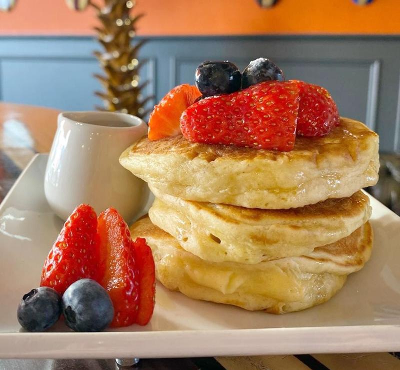 Stack of fluffy pancakes topped with strawberries and blueberries, served with syrup