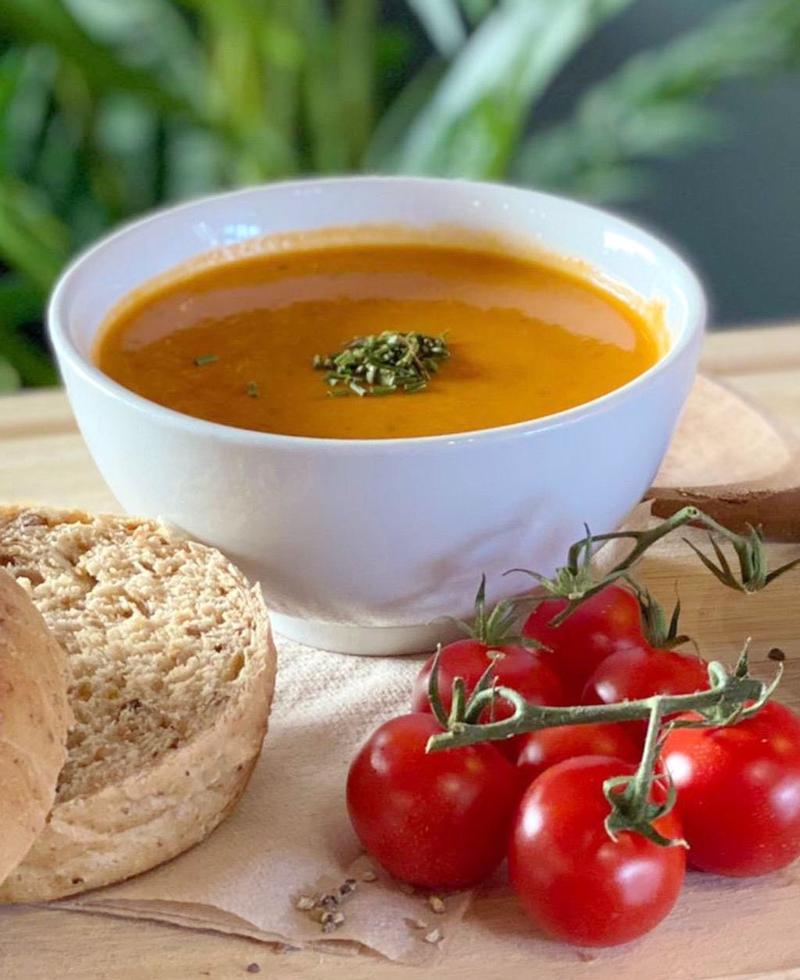 Tomato soup garnished with herbs, served with cherry tomatoes and a bread roll