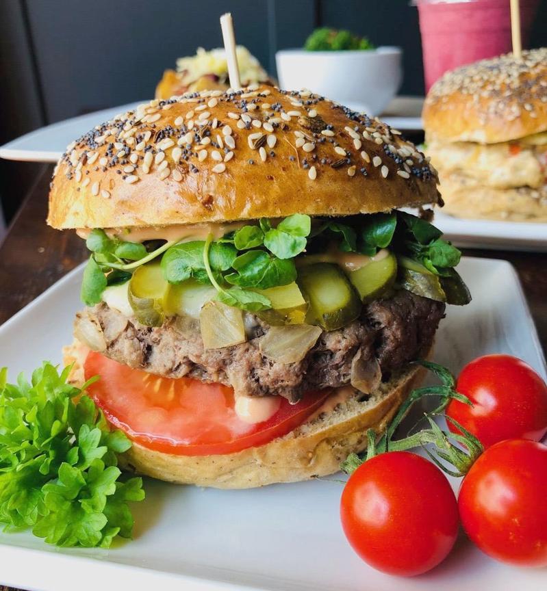 Gourmet burger with tomato, pickles, watercress in a seeded bun, served with cherry tomatoes